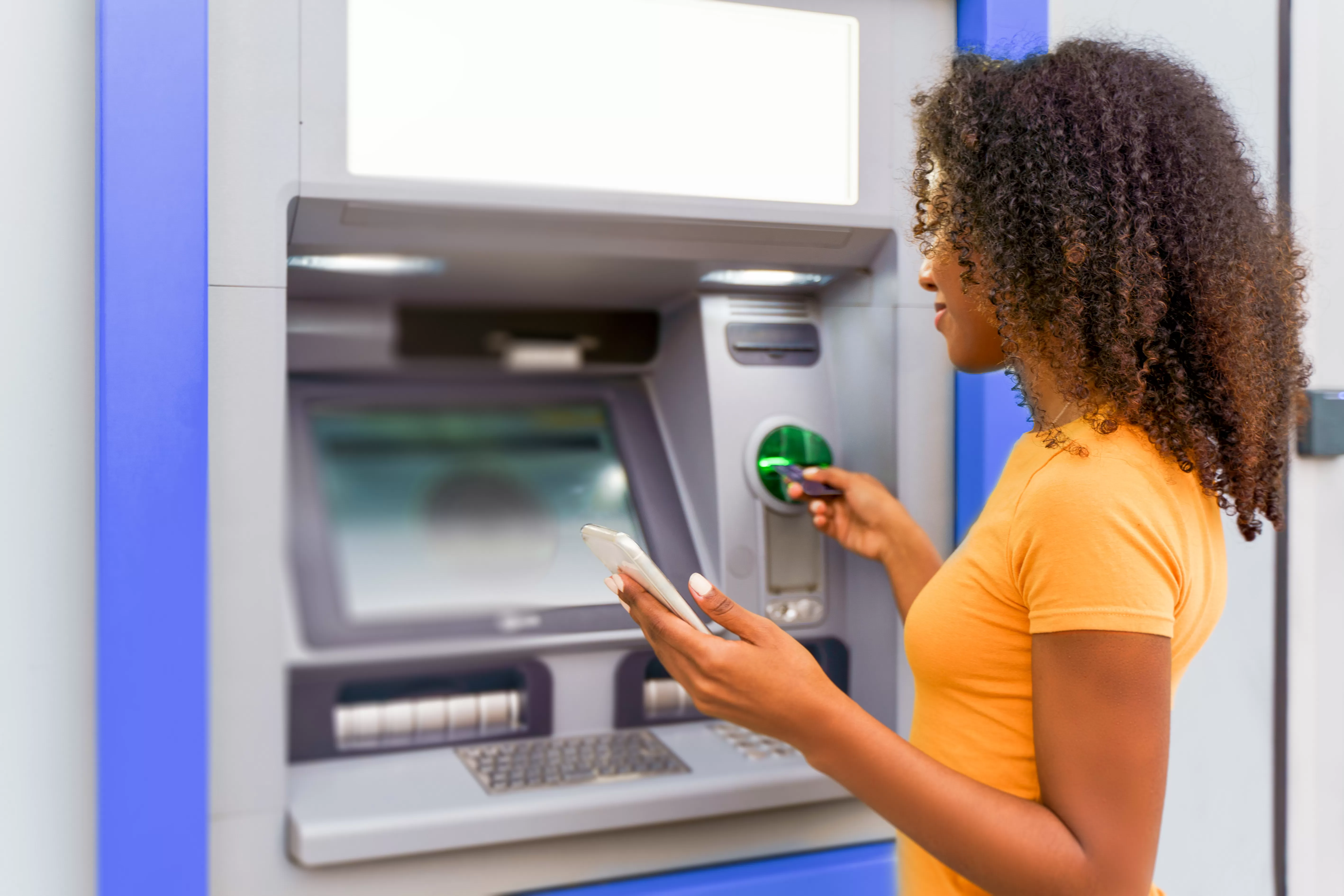 woman inserting debit card at ATM and holding phone