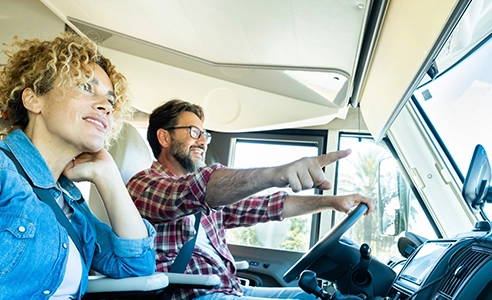 Adult couple traveling with home vehicle camper cabin. Man pointing destination at woman.